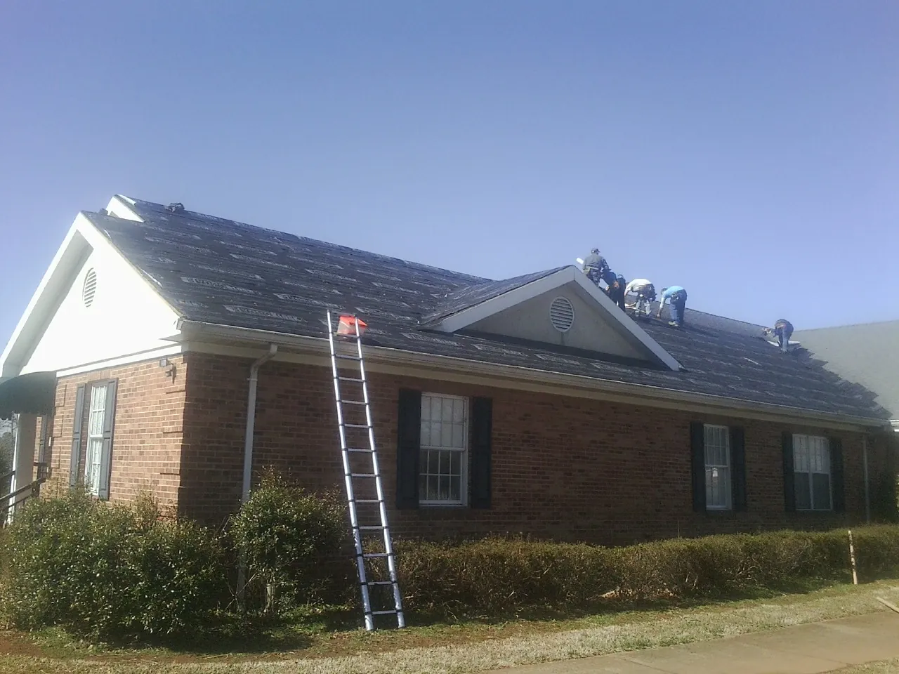Crew tearing shingles off a brick ranch roof with a ladder set — Emergency Roof Repair work by our crew in Owingsville