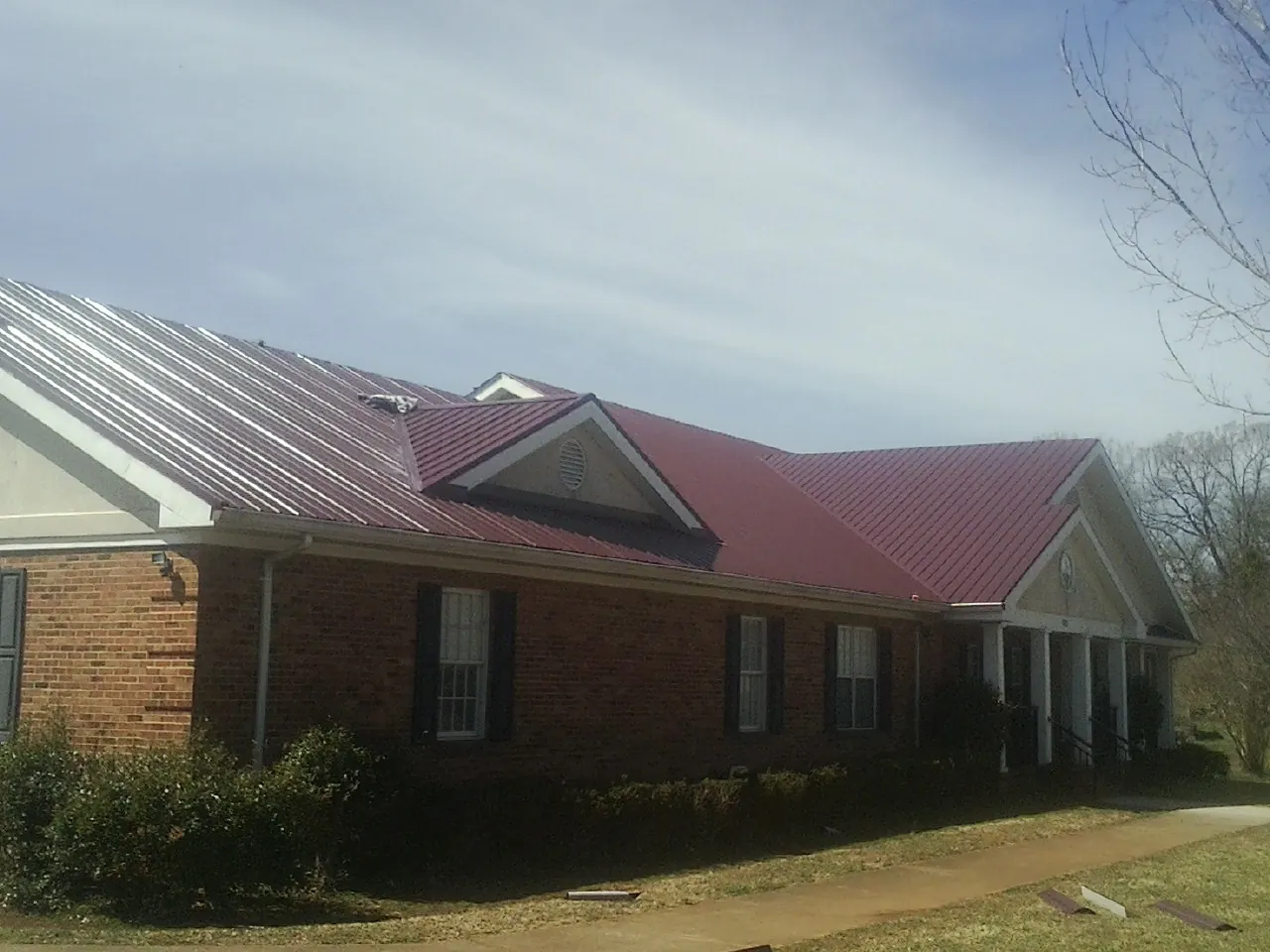 Red metal roof with gabled entries on a long brick building, from a Hail Damage Roof Repair job in Owingsville