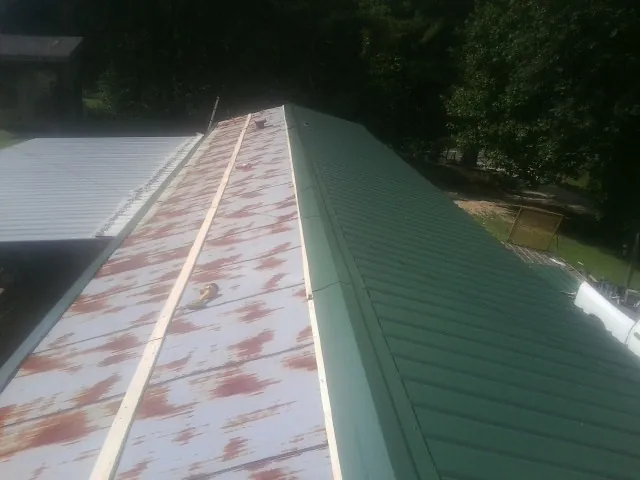 Old rusted panels beside newly installed green metal roofing — Wind Damage Roof Repair by Roofing Brothers in Owingsville