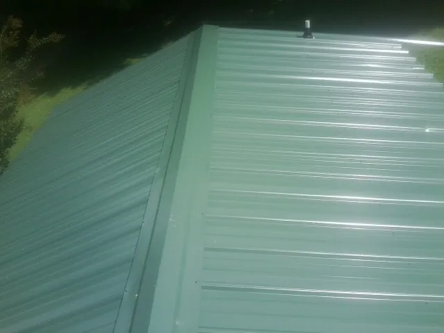 New green metal panels meeting at the ridge of a roof — Flat Roof Repair work by our crew in Owingsville