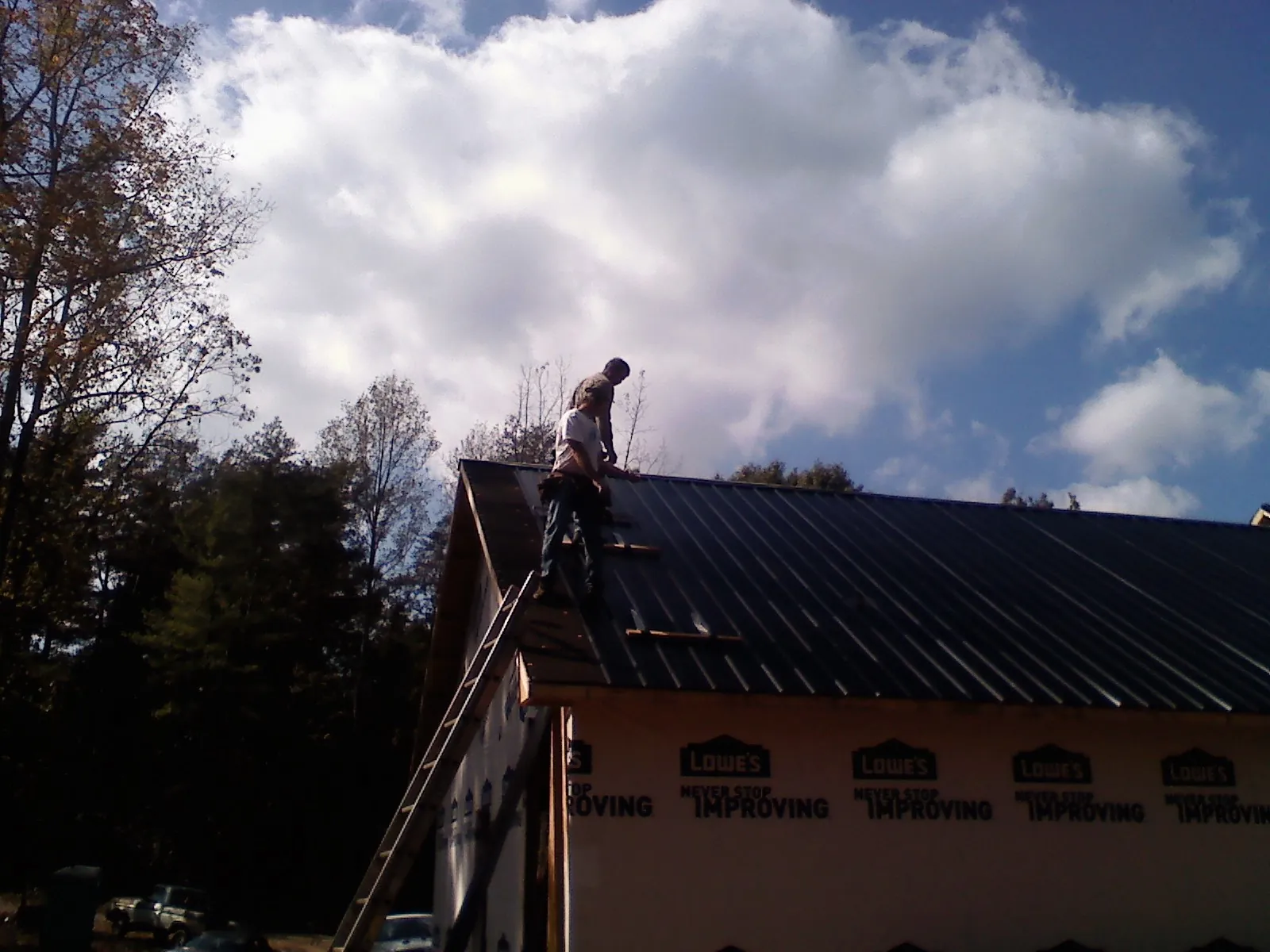 Roofer fastening dark metal panels high against a cloudy sky, from a Roof Inspection job in Owingsville