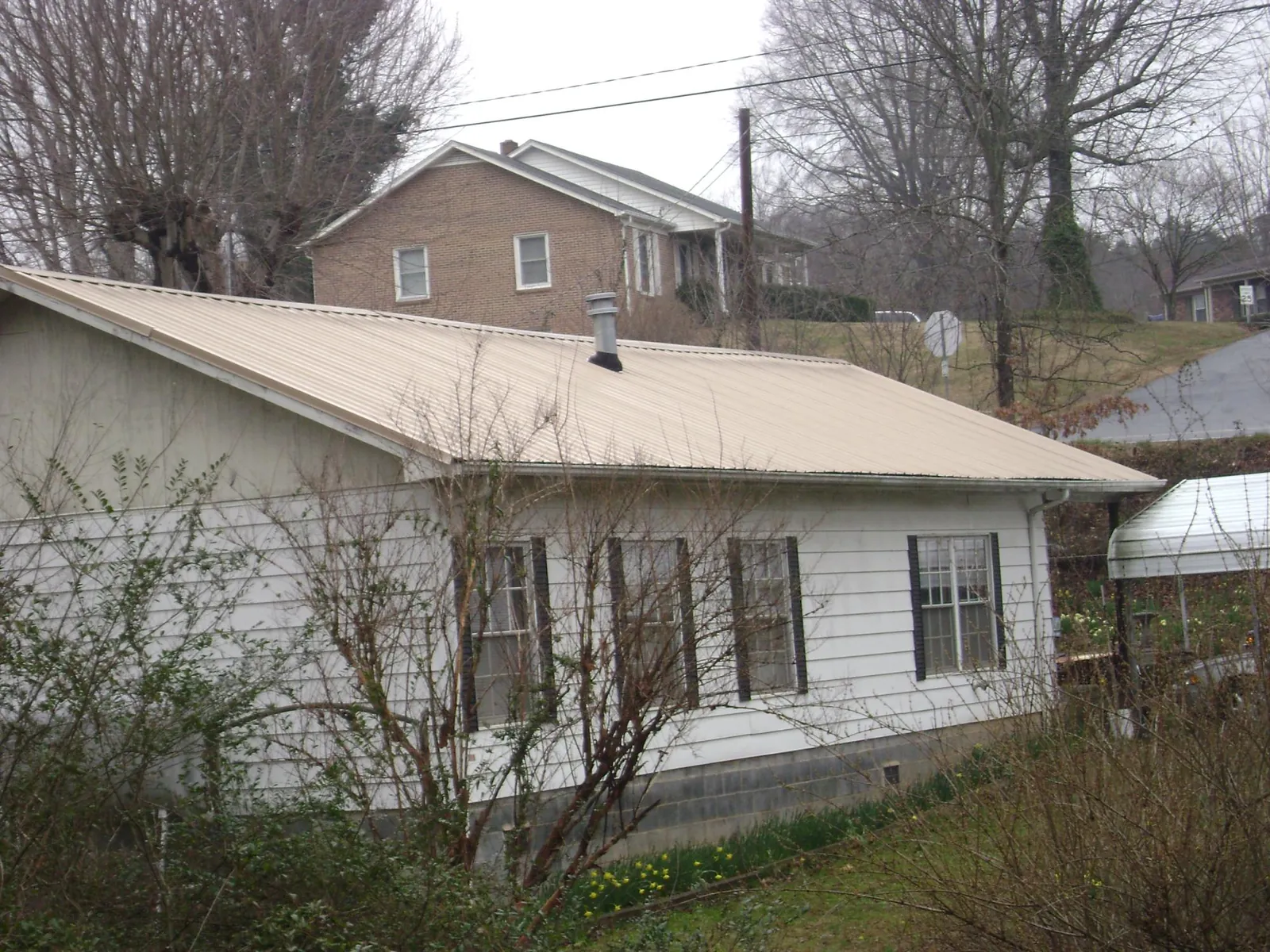 Tan metal roof on a white sided house set into a hillside — Commercial Roofing by Roofing Brothers in Owingsville
